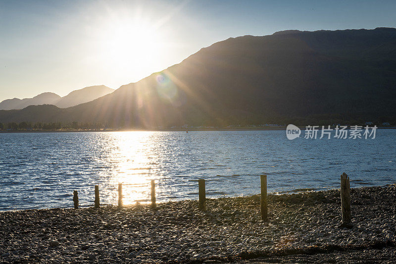 从苏格兰格伦科的布里林荷湖(Loch Linnhe)岸边望去，太阳正从阿德古尔半岛的山脉后面落下。